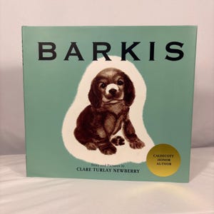 May include: A children's book titled "Barkis" with a brown puppy illustration on a light green background. The book cover features the title in large black letters and the author's name. A gold sticker indicates the Caldecott Honor Author.