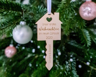 May include: A wooden Christmas ornament shaped like a house key with the text "Unser erstes Weihnachten im neuen Zuhause 2020" and "Sandra & Daniel" on it.
