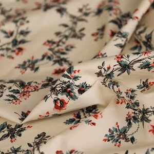 May include: White cotton fabric with a repeating floral pattern. The flowers are red and pink with green leaves. The fabric is soft and has a subtle sheen.