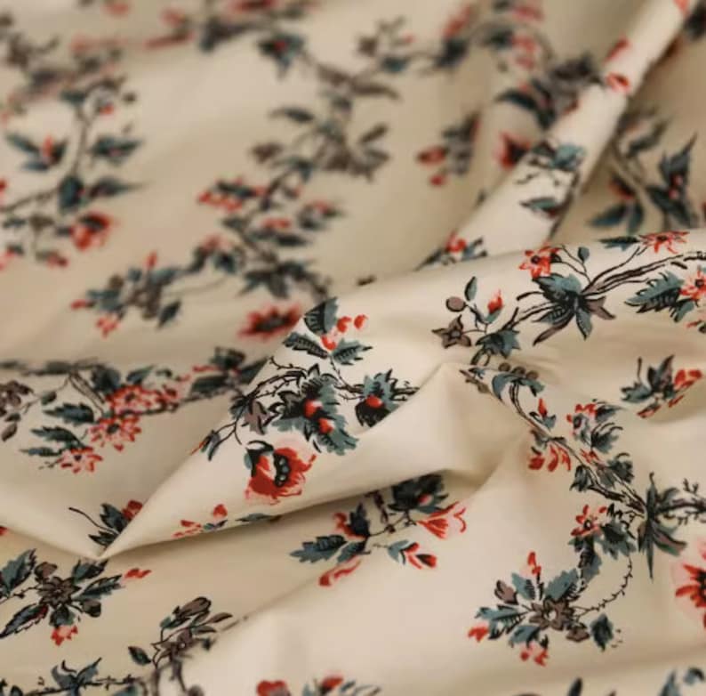 May include: White cotton fabric with a repeating floral pattern. The flowers are red and pink with green leaves. The fabric is soft and has a subtle sheen.