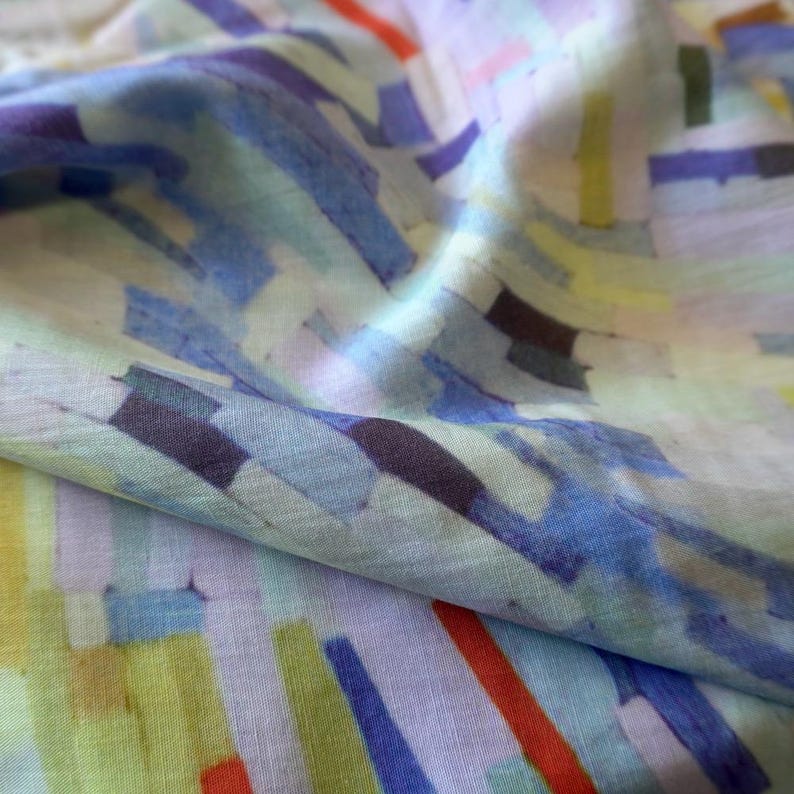 May include: Close-up of a fabric with a colorful abstract pattern. The design features overlapping rectangular shapes in shades of blue, green, yellow, purple, and red. The fabric has a soft, flowing appearance.