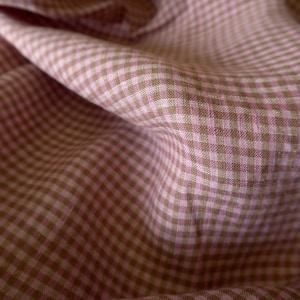 May include: A close-up of a pink and brown gingham fabric. The fabric is woven with a small checkered pattern and has a soft, textured feel.