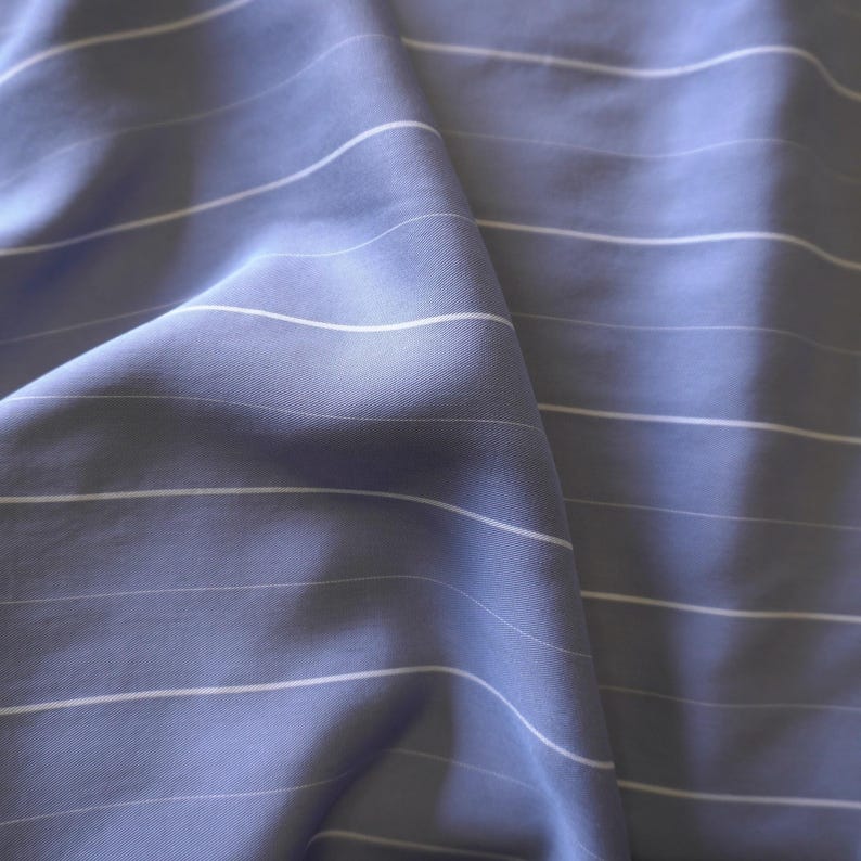 May include: A close-up of a blue and white striped fabric. The fabric is soft and has a subtle sheen.