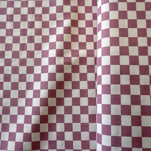 May include: A close-up of a fabric with a chequered pattern. The pattern features alternating squares of white and a muted reddish-purple colour. The fabric is folded, showing the pattern on the front and the side.