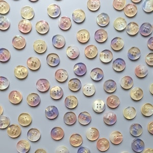 May include: Assortment of iridescent oval buttons in various shades of pink, purple, and yellow. The buttons have four holes each.