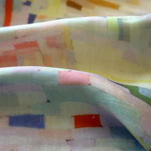 May include: Close-up of fabric with an abstract pattern. The fabric features a mix of pastel colors, including pink, blue, yellow, and green, arranged in rectangular shapes. The fabric appears soft and flowing, with subtle folds and textures.