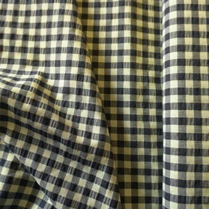 May include: Close-up of a fabric with a classic gingham pattern. The fabric features a repeating grid of navy blue and cream-coloured squares. The fabric is slightly textured and appears to be folded, creating shadows and depth.