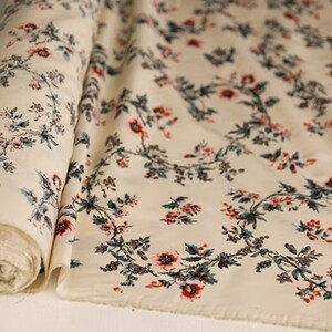 May include: Cream-colored fabric with a repeating floral pattern. The flowers are red and pink with green leaves. The fabric is rolled up and the pattern is visible on both sides.