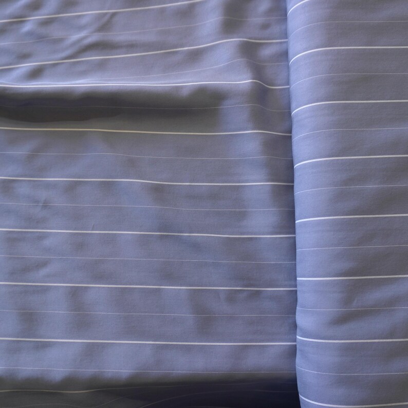 May include: A close-up of a blue and white striped fabric. The fabric is folded in half and the stripes are running vertically.