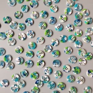 May include: A collection of colourful buttons with a variety of abstract patterns in shades of blue, green, and white.