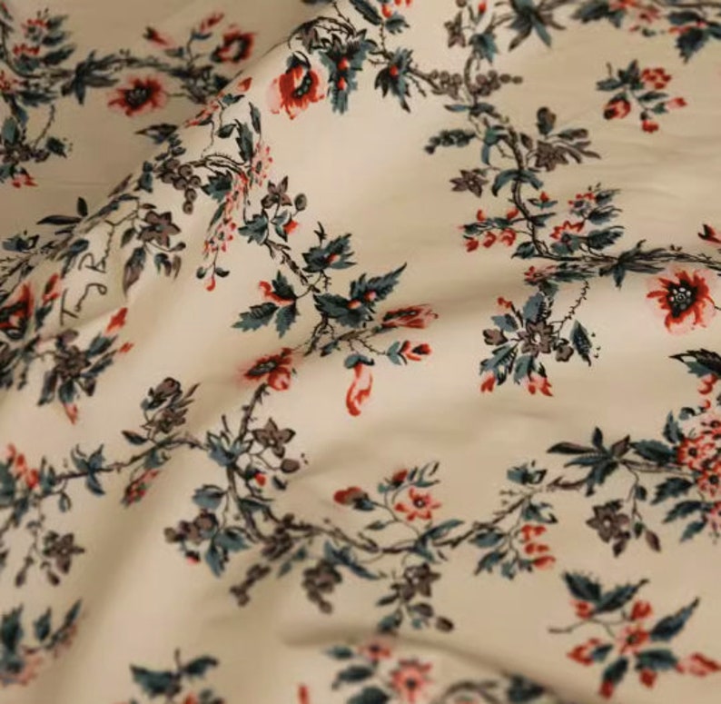 May include: White fabric with a repeating floral pattern. The flowers are red and pink with green leaves.