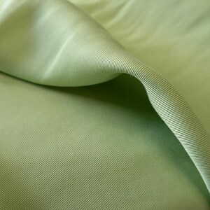 May include: Close-up of a folded section of light green fabric. The fabric has a ribbed texture with diagonal lines running across the surface. The fabric is smooth and appears to be a lightweight material, possibly cotton or a blend.