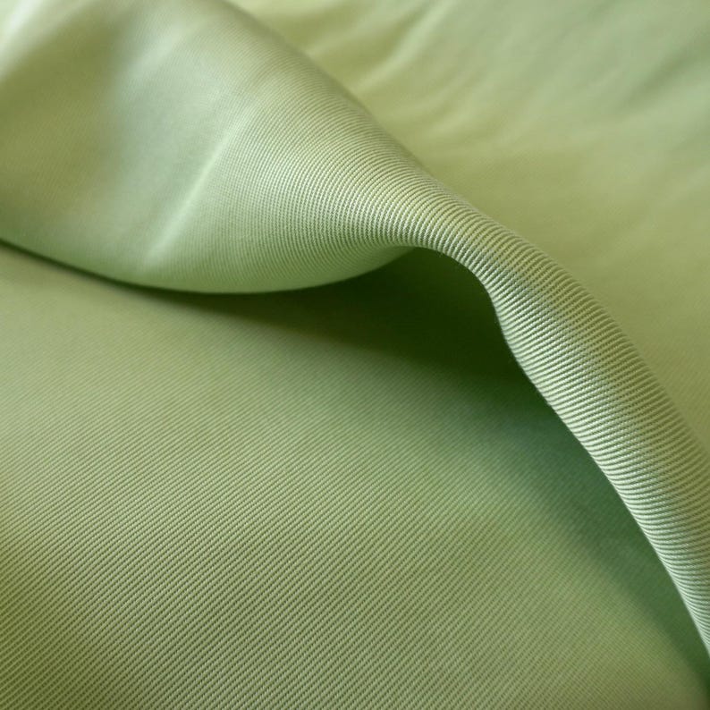 May include: Close-up of a folded section of light green fabric. The fabric has a ribbed texture with diagonal lines running across the surface. The fabric is smooth and appears to be a lightweight material, possibly cotton or a blend.
