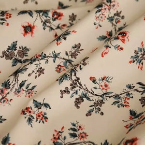 May include: A white fabric with a repeating pattern of small red and gray flowers on a vine. The fabric has a subtle sheen and a soft texture.