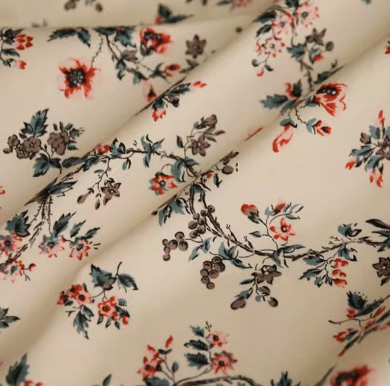 May include: A white fabric with a repeating pattern of small red and gray flowers on a vine. The fabric has a subtle sheen and a soft texture.