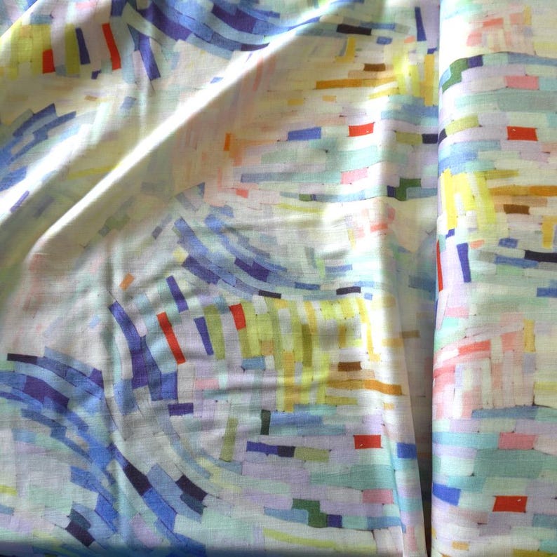 May include: Abstract fabric with a colorful pattern. The design features a mix of blue, yellow, red, and green rectangular shapes and curved lines on a white background. The fabric is folded, showing its texture and drape.