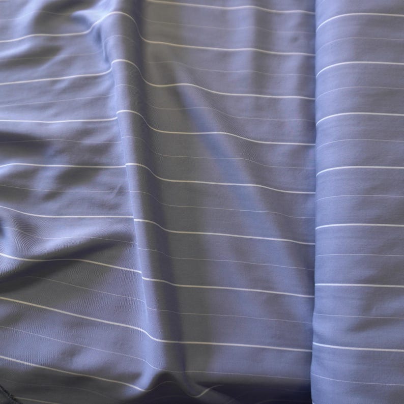 May include: A close-up of a light blue fabric with white stripes. The fabric is folded and has a smooth texture.