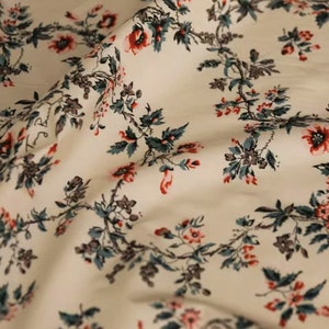 May include: White fabric with a repeating floral pattern. The flowers are red and pink with green leaves. The fabric has a subtle texture.