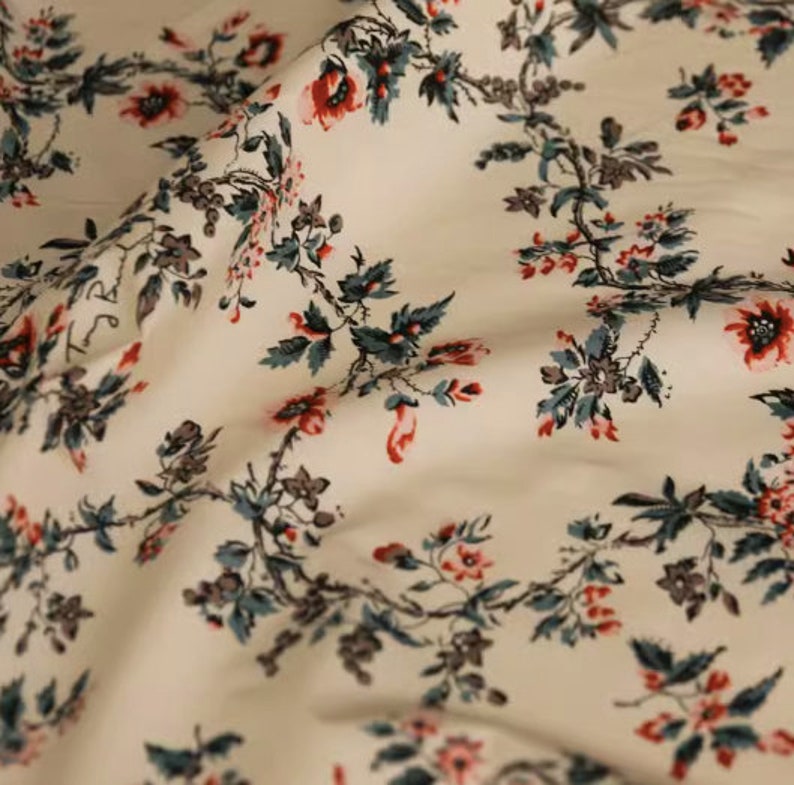 May include: White fabric with a repeating floral pattern. The flowers are red and pink with green leaves. The fabric has a subtle texture.