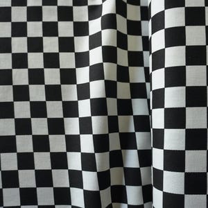 Könnte beinhalten: Nahaufnahme eines Stoffes mit einem schwarz-weißen Schachbrettmuster. Der Stoff ist drapiert und zeigt Falten und Textur. Die abwechselnden Quadrate erzeugen ein kühnes, grafisches Design, das für verschiedene Bastel- und Nähprojekte geeignet ist.