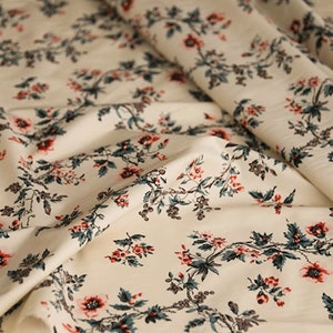 May include: White fabric with a repeating pattern of red and green floral sprigs. The fabric has a subtle texture and a soft, flowing drape.
