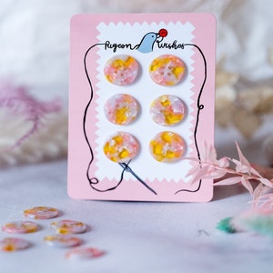May include: Six pink and yellow swirl buttons on a pink card with the text "Pigeon Wishes".