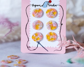 Puede incluir: Seis botones de espiral rosa y amarillo en una tarjeta rosa con el texto "Pigeon Wishes".