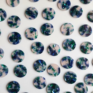 May include: Assortment of round, blue, green and white patterned buttons. The buttons have a mottled, marbled appearance.