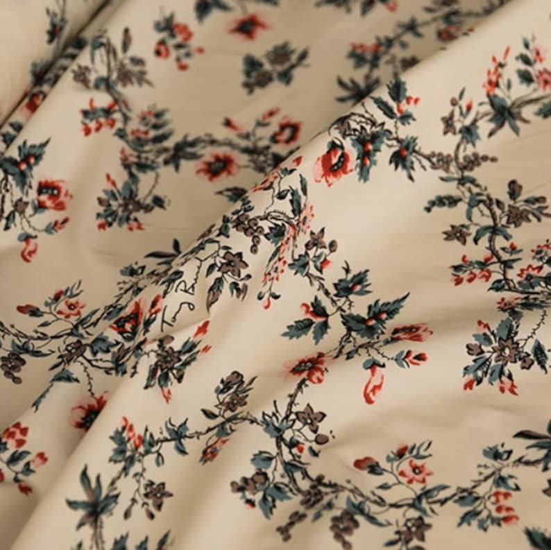 May include: White fabric with a repeating pattern of red and green floral sprigs. The fabric has a subtle sheen and a soft texture.