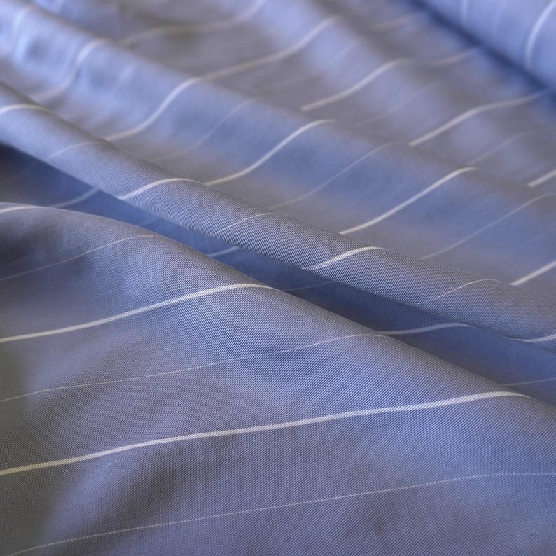 May include: A close-up of a blue fabric with white stripes. The fabric is wrinkled and has a soft texture.