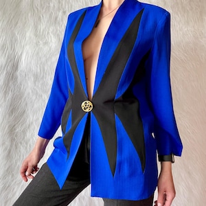 Puede incluir: Una llamativa blazer azul con detalles geométricos negros y cierre de botón dorado. La chaqueta de manga larga presenta un diseño de cuello en V. Una pieza audaz y elegante.