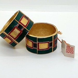 May include: Two gold-coloured metal bangle bracelets. Each bracelet has a geometric design with green, red, and gold rectangular shapes. The bracelets have a hinged closure. A tag with the brand name "LANVIN PARIS" is attached.