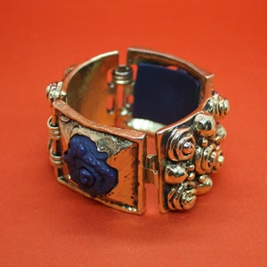 Könnte beinhalten: Ein goldfarbenes Armreif-Armband mit einem blauen Rosenmuster. Das Armband ist mit einem Scharnier versehen und lässt sich zum Anlegen am Handgelenk öffnen.