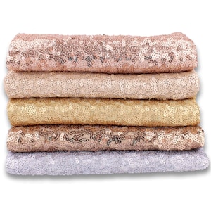 May include: A stack of five rolls of sparkly fabric in various shades of gold, rose gold, and silver. The fabric is made of sequins and is perfect for crafting, decorating, or adding a touch of glamour to any project.