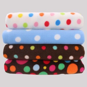 May include: Four fleece blankets stacked on top of each other. The top blanket is white with colourful polka dots. The second blanket is light blue with white polka dots. The third and fourth blankets are brown with colourful polka dots.
