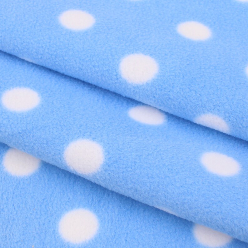 May include: Close-up of a blue fabric with white polka dots. The fabric is folded in thirds, showing the pattern on each layer.
