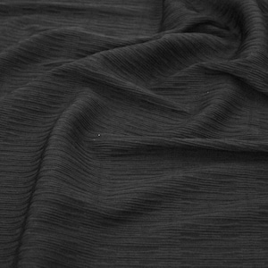 May include: Black fabric with a crinkled texture. The fabric is folded and draped, creating soft folds and wrinkles.