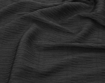 May include: Black fabric with a crinkled texture. The fabric is folded and draped, creating soft folds and wrinkles.