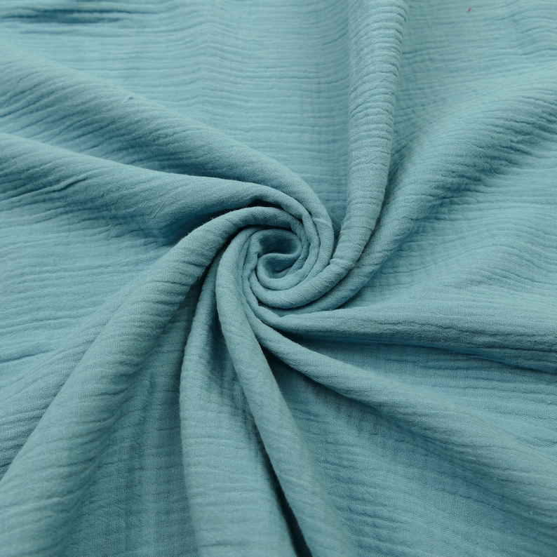 Pu&ograve; includere: Un primo piano di un tessuto morbido e blu con una texture stropicciata. Il tessuto &egrave; piegato e drappeggiato, creando uno schema a spirale.
