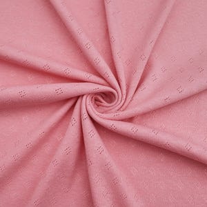 Puede incluir: Primer plano de una tela de punto rosa con un peque&ntilde;o patr&oacute;n de rombos. La tela tiene un tacto suave y texturizado, ideal para proyectos de costura.