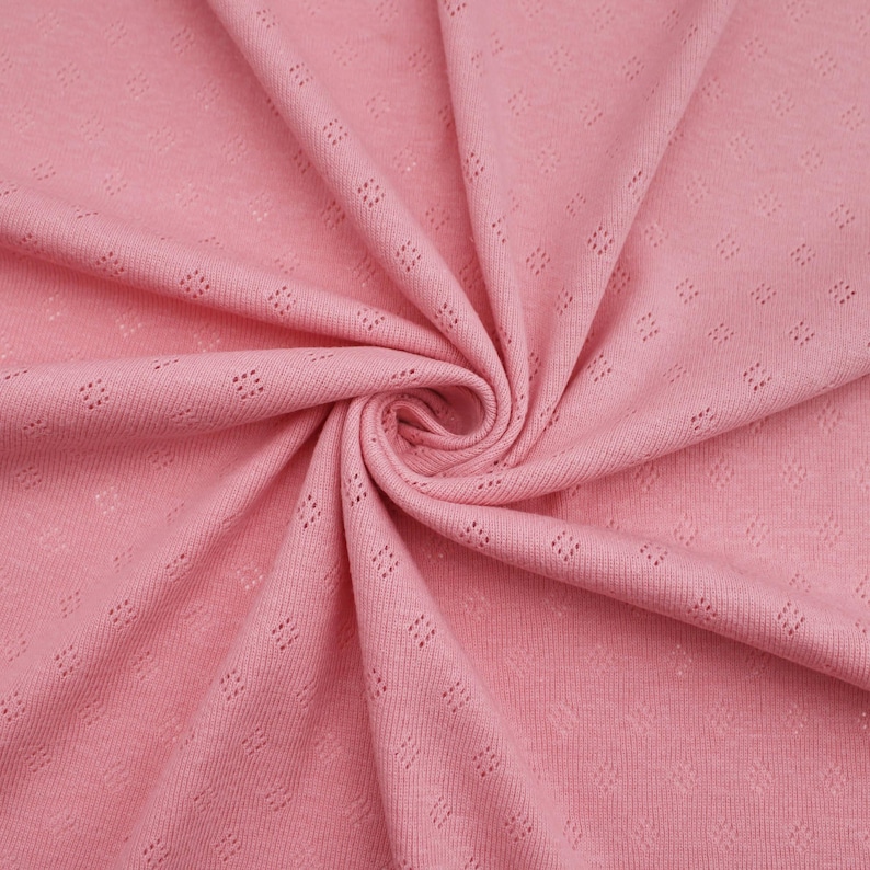 Puede incluir: Primer plano de una tela de punto rosa con un peque&ntilde;o patr&oacute;n de rombos. La tela tiene un tacto suave y texturizado, ideal para proyectos de costura.