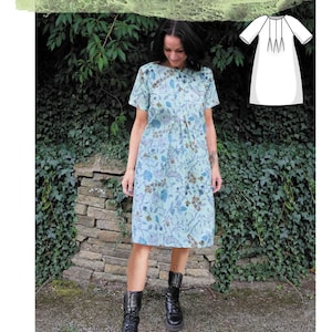 May include: A woman wearing a light blue floral dress with short sleeves and a round neckline. The dress has a gathered waist and a knee-length skirt. The woman is standing in front of a stone wall covered in green ivy. The image includes the text "Layer Up Triple Tuck Smock" and "Sew Different".