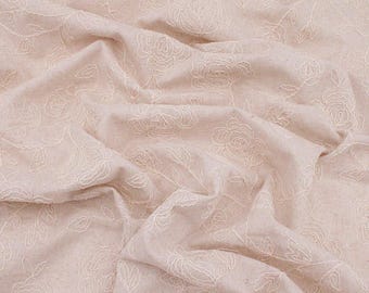 May include: Close-up of a beige fabric with an embroidered floral pattern. The design features detailed outlines of roses and leaves, creating a textured surface. The fabric is gathered, showing the folds and shadows.