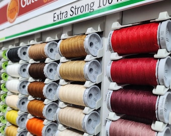 Puede incluir: Primer plano de una variedad de carretes de hilo en diferentes colores, incluyendo rojo, marrón, beige y blanco. Los carretes están etiquetados "Extra Strong 100 m" y "Gütermann creativ".