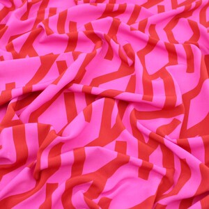 Peut inclure: Tissu rose vif avec un motif répétitif de formes géométriques orange. Le tissu est drapé, créant des plis doux et des ombres. La combinaison de couleurs audacieuses et le design suggèrent une esthétique moderne.