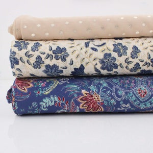 Könnte beinhalten: Drei Stoffmuster, die übereinander gestapelt sind. Das oberste Muster ist hellbeige mit kleinen silbernen Punkten. Das mittlere Muster ist cremefarben mit einem blauen Blumenmuster. Das unterste Muster ist dunkelblau mit einem Paisley-Muster.