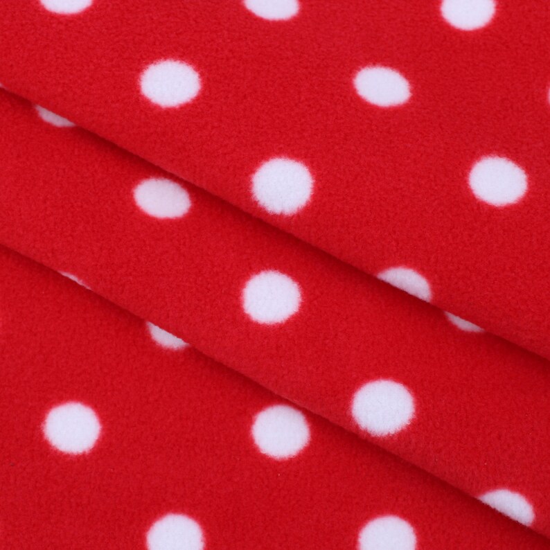 May include: Red fleece fabric with white polka dots. The fabric is folded in thirds, showing the pattern on both sides.