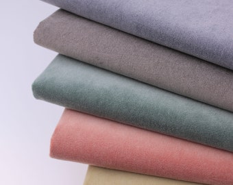 May include: A stack of five fabric swatches in different colors. The swatches are arranged from lightest to darkest, with the top swatch being a light purple, followed by a light brown, a light green, a light pink, and a light beige.