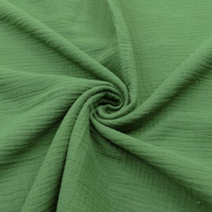 Pu&ograve; includere: Un primo piano di un tessuto verde con una superficie testurizzata e stropicciata. Il tessuto &egrave; piegato e drappeggiato, mostrando la sua natura morbida e flessibile.