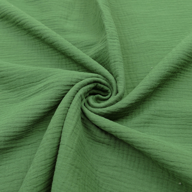 Pu&ograve; includere: Un primo piano di un tessuto verde con una superficie testurizzata e stropicciata. Il tessuto &egrave; piegato e drappeggiato, mostrando la sua natura morbida e flessibile.